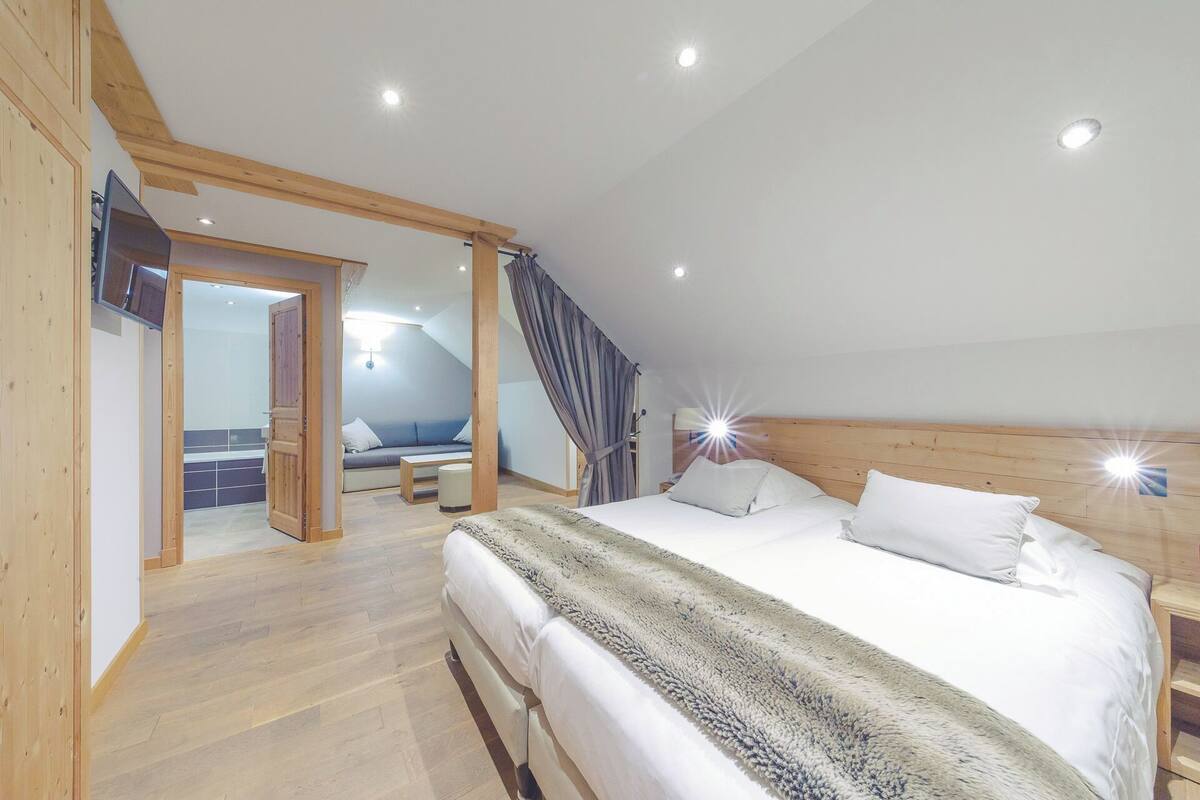 A bedroom with a large bed, wooden ceiling beams, and a view of the bathroom.