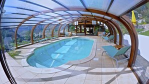 A covered swimming pool with lounge chairs and a glass ceiling. - Fleur De Neige Hôtel (Chatel)