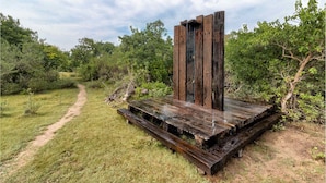 A rustic wooden structure with a bench, surrounded by greenery and a dirt path. - Kodev (Kalpitiya)