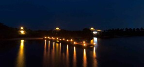 A nighttime view of a dock with lights reflecting on the water, surrounded by trees. - Kodev (Kalpitiya)