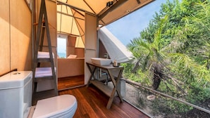 A compact bathroom with a toilet, sink, and shower area, featuring a wooden floor and a view of lush greenery. - Kodev (Kalpitiya)