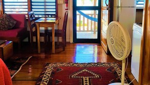 Una sala de estar acogedora con techo de madera, una mesa de comedor con sillas, un sofá, un tapete estampado y un ventilador.