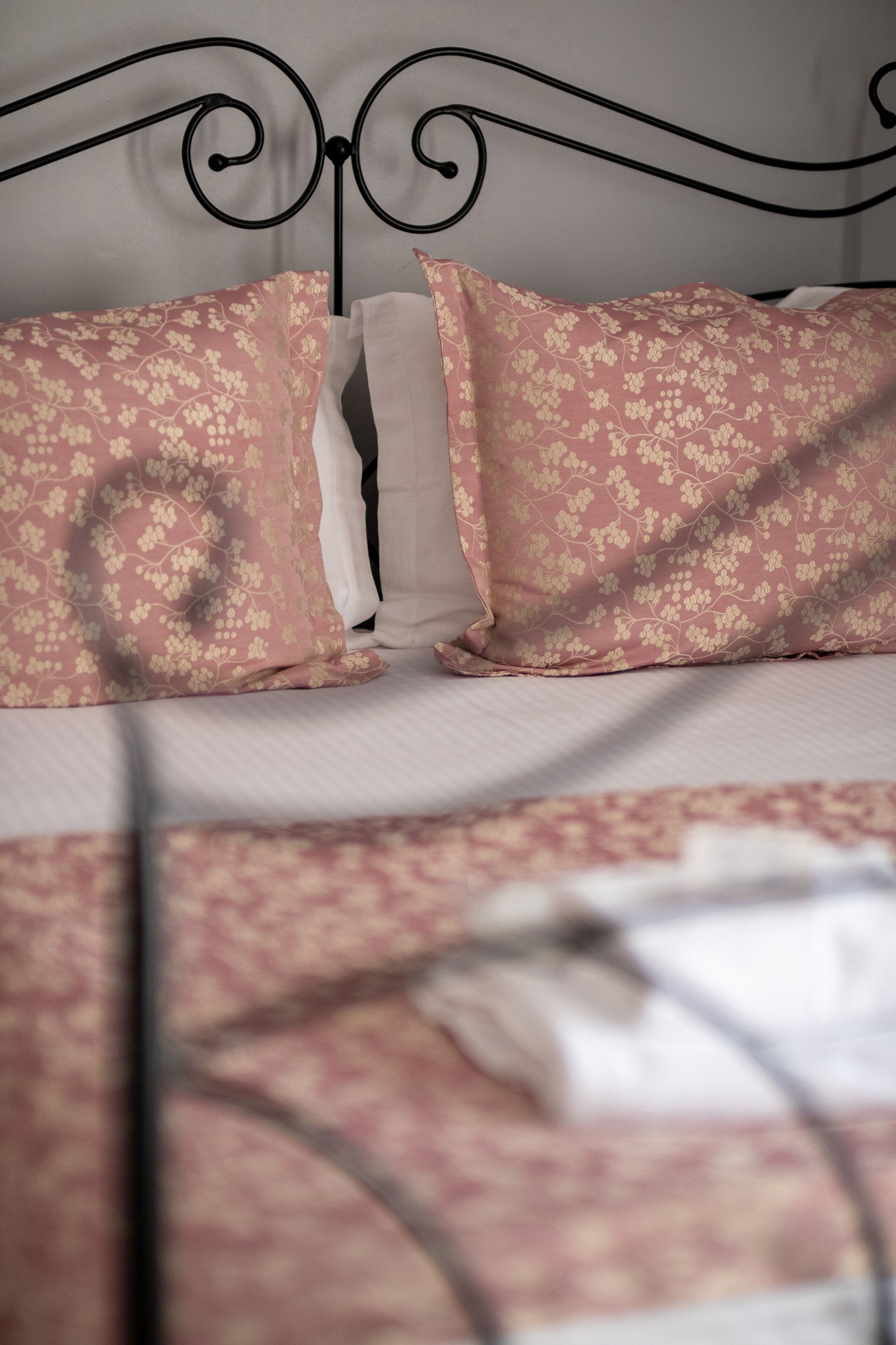 A bed with a metal headboard, two pink floral pillows, and a white pillow.