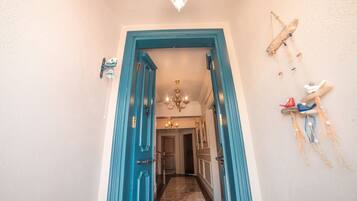 Corredor com porta azul que dá para um quarto. É possível ver um candelabro e elementos decorativos nas paredes.