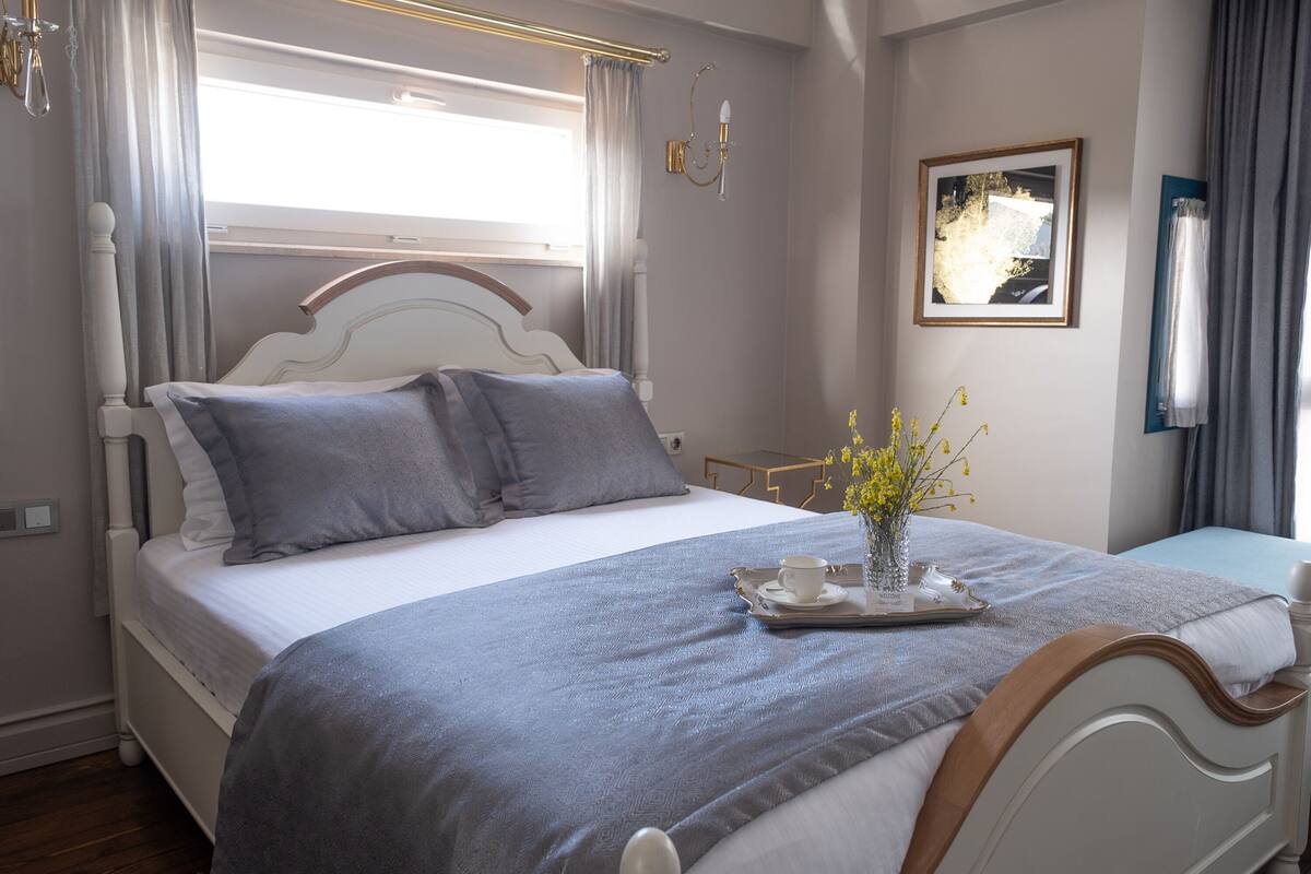 A neatly made bed with a tray of breakfast items, a vase with flowers, and a framed picture on the wall.