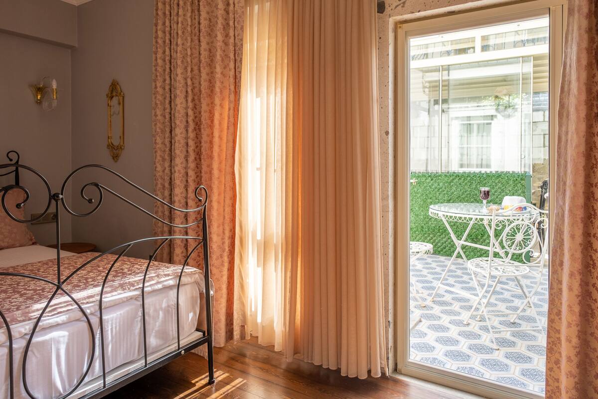 A bedroom with a bed, curtains, and a view of an outdoor patio with a table and chairs.