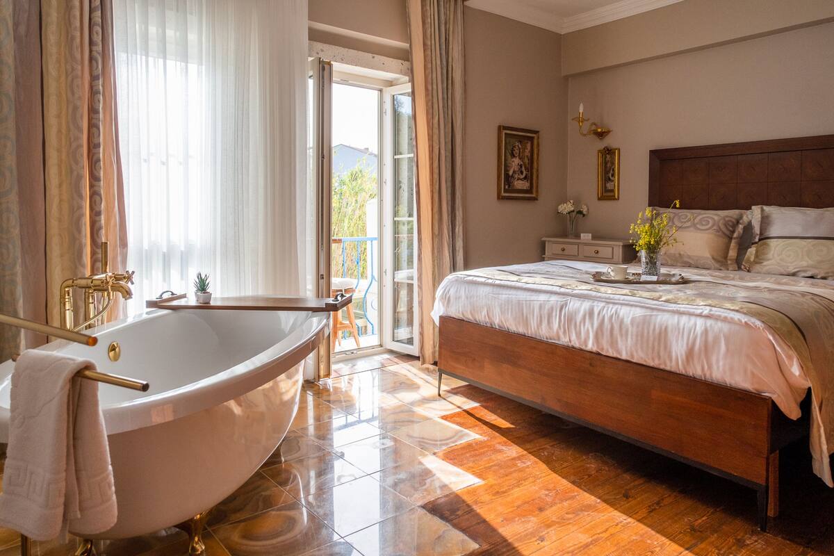 A bedroom with a large bed, a bathtub, and a balcony with a view.