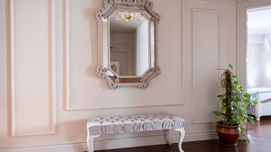Una habitación con un banco blanco, un espejo grande y ornamentado, y una planta en maceta.