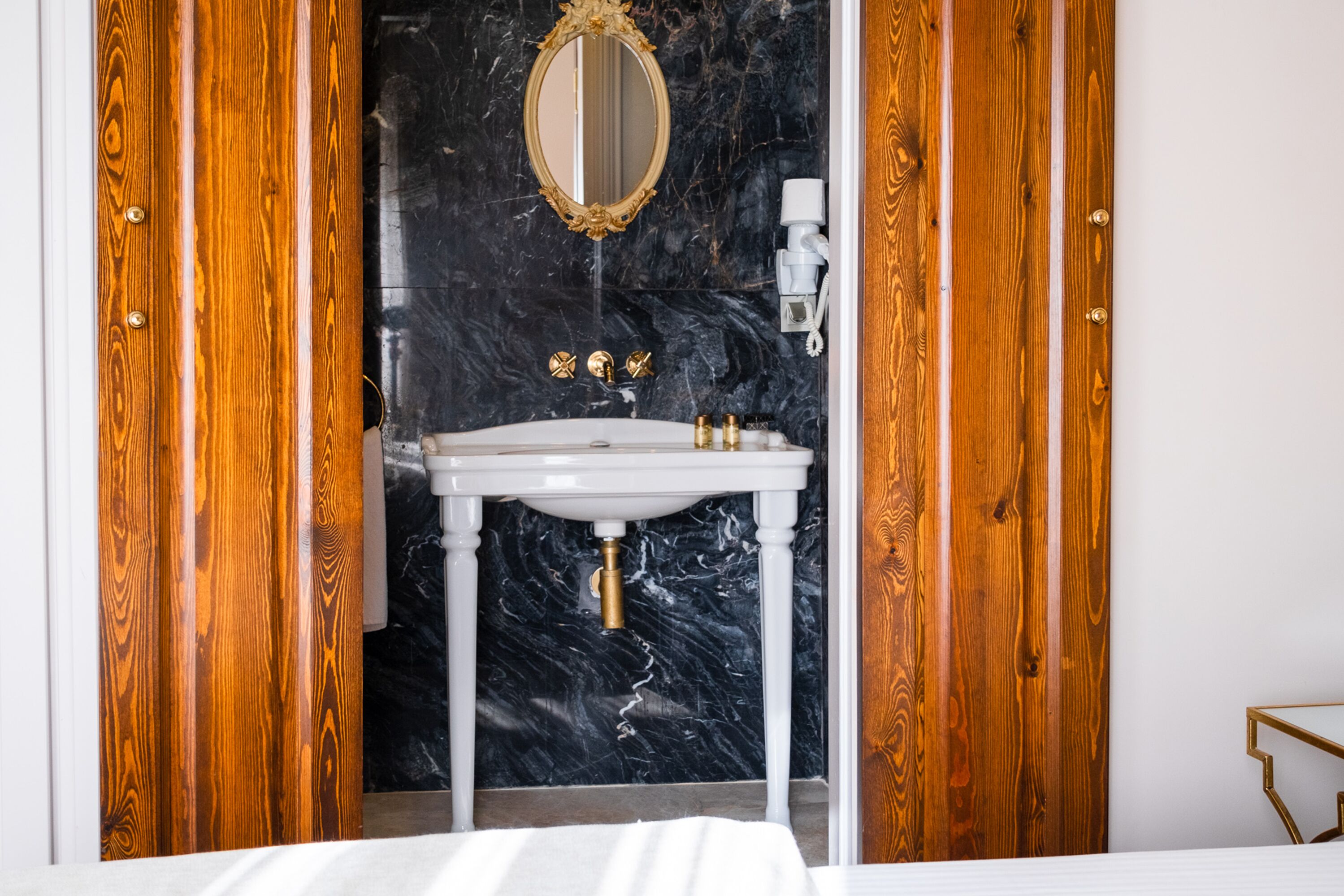 A bathroom with a marble sink, wooden doors, and a gold-framed mirror.