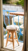 A wooden stool with a cushion on a balcony with blue railings.