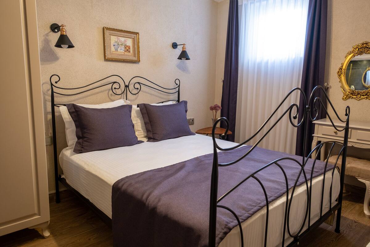 A neatly made bed with a metal frame, a bedside table with a lamp, and a mirror on the wall.
