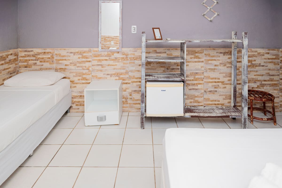 A room with two beds, a small bedside table, a mirror, and a storage unit with a refrigerator.