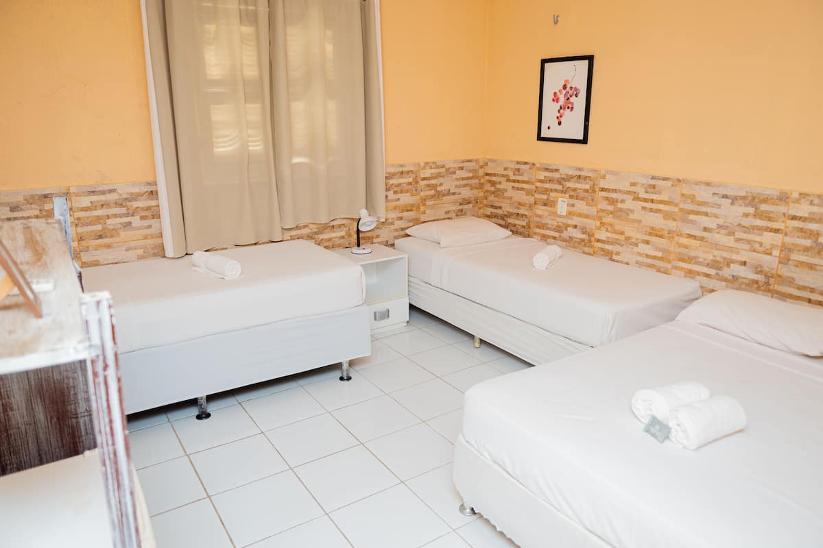 A hotel room with two single beds, a small bedside table with a lamp, a window with curtains, and a wall-mounted picture.