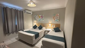 Habitación de hotel con dos camas, una mesita de noche pequeña, aire acondicionado montado en la pared y dos obras de arte florales.