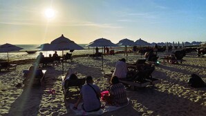 Una playa con sombrillas y sillas reclinables, cielo despejado y el sol poniéndose o saliendo.