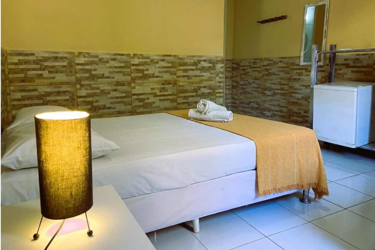 A hotel room with a bed, a bedside lamp, a towel, a small table, and a mirror.