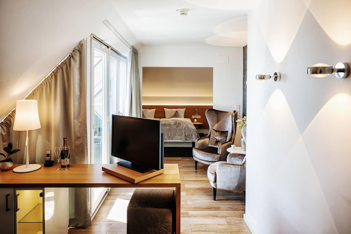 A modern hotel room with a wooden desk, a flat-screen TV, a comfortable sofa, and a bed with a headboard.