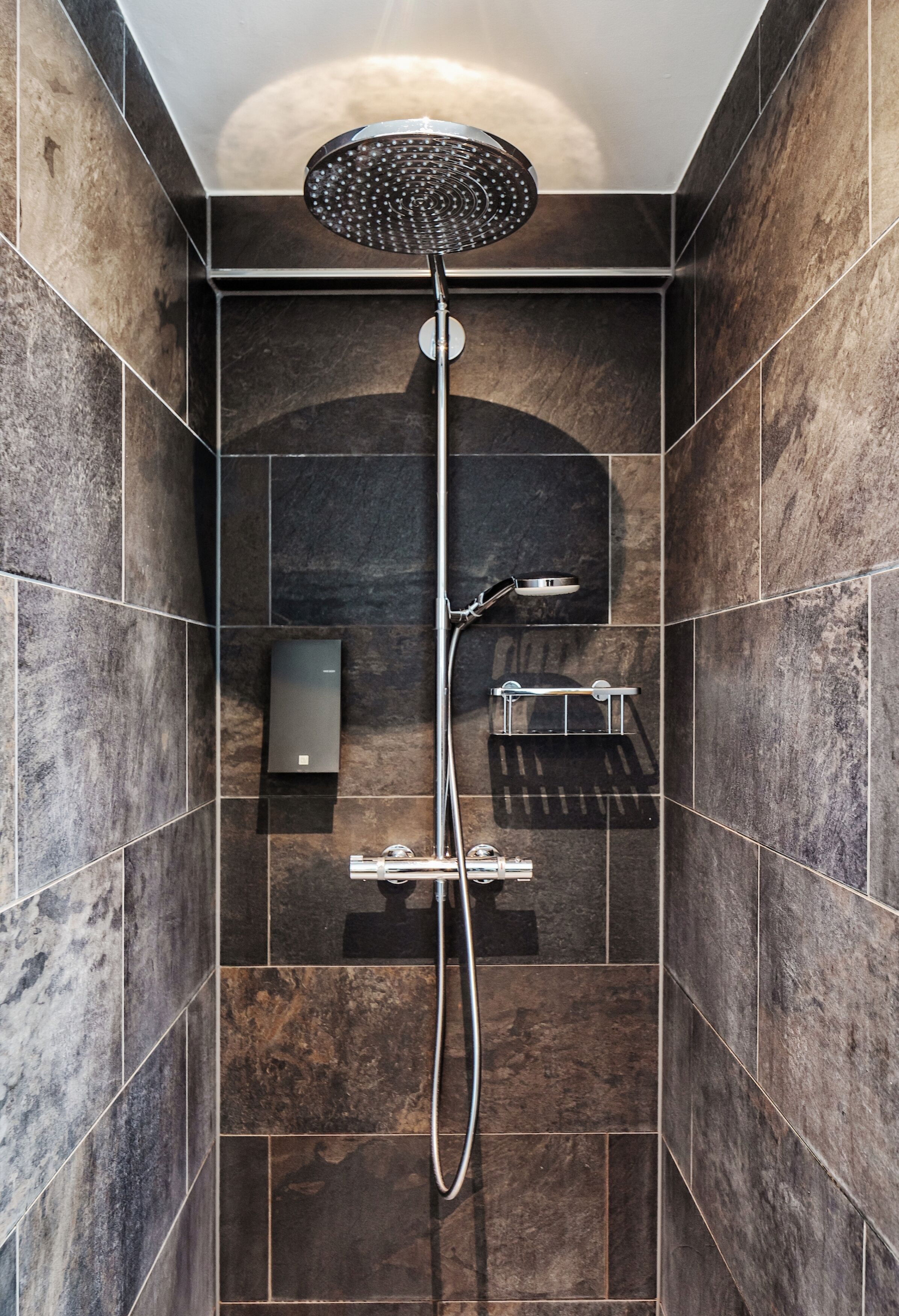 A modern shower with a rain showerhead, a handheld showerhead, and a wall-mounted control panel.