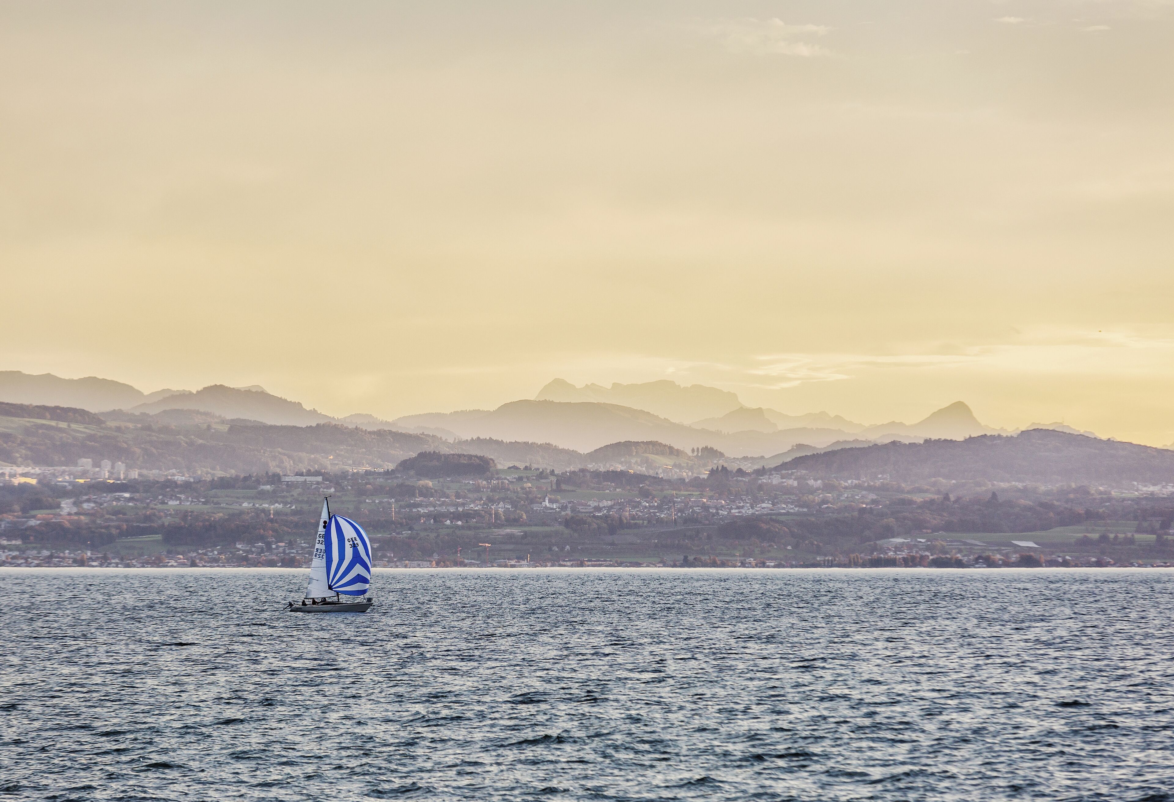 Ein Segelboot auf ruhigem Wasser, im Hintergrund eine gebirgige Landschaft.