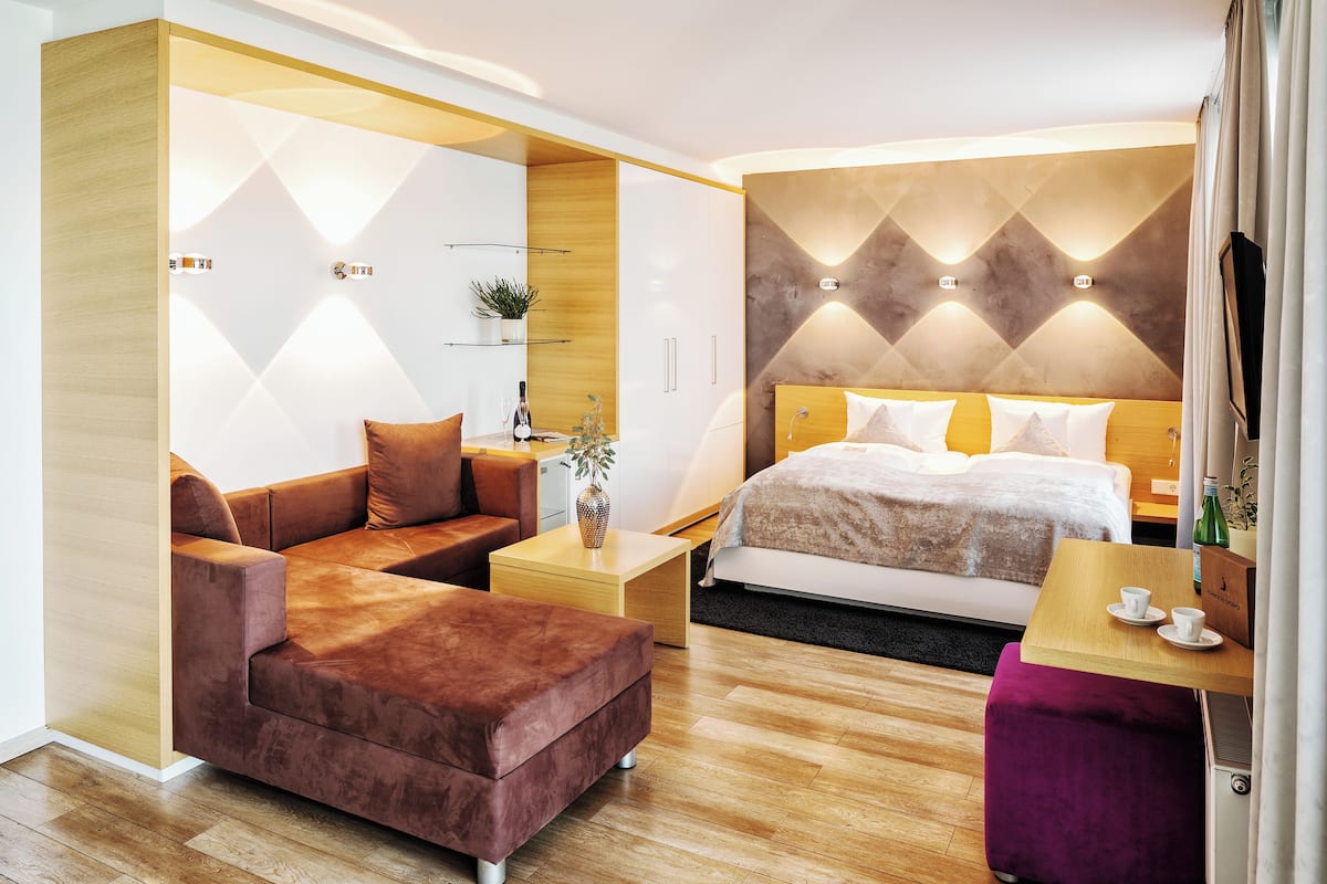A modern hotel room with a sofa, a small table, a bed, and a wooden accent wall.