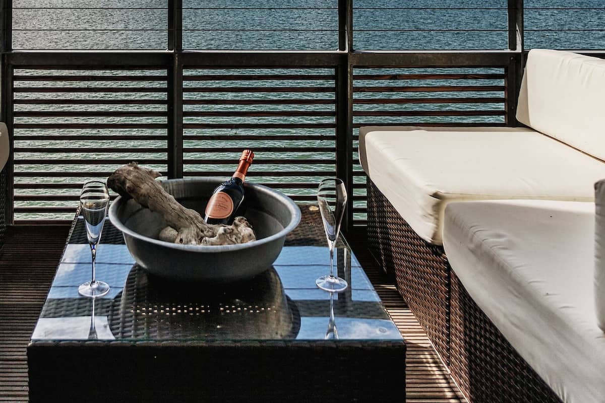 A balcony with a view of the sea, a bottle of champagne, and a glass on a table.