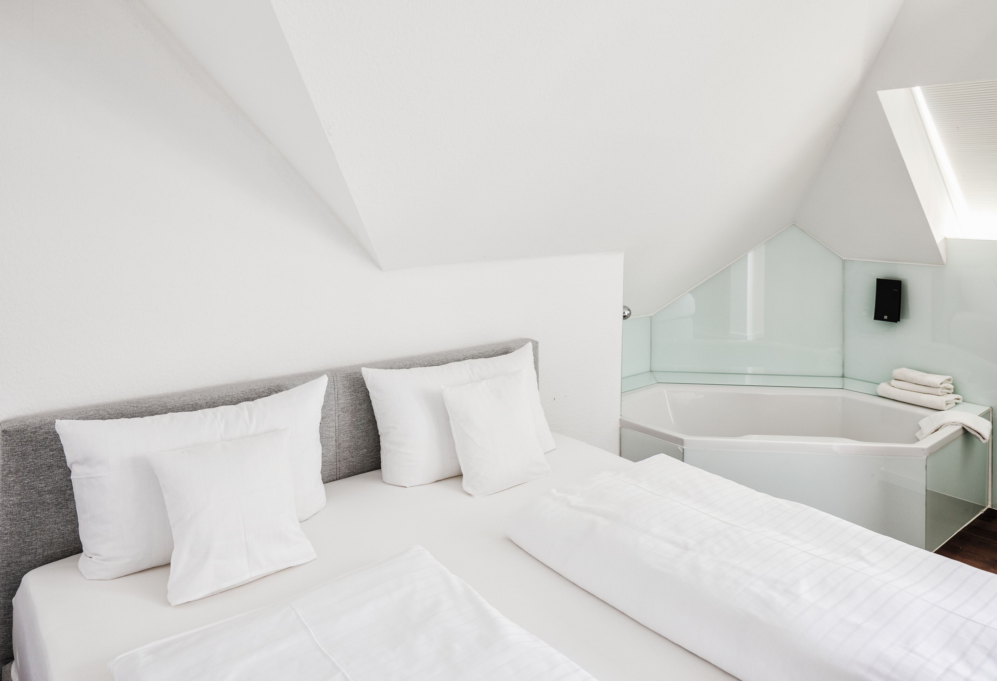 Un dormitorio moderno con una cama grande, una bañera con cristal y un tragaluz.