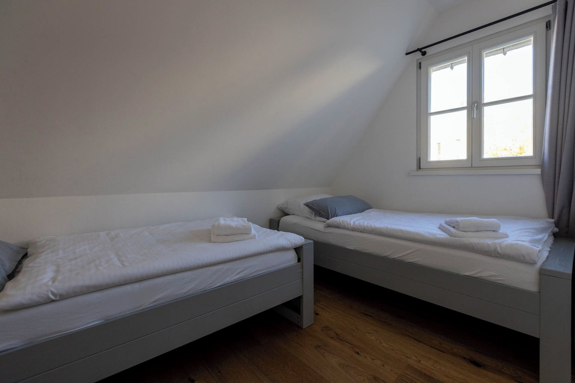 Ein Zimmer mit zwei Einzelbetten, einem Fenster mit Vorhängen und Holzboden.