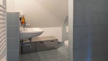 Une salle de bain moderne avec un lavabo blanc, des toilettes et un espace douche.