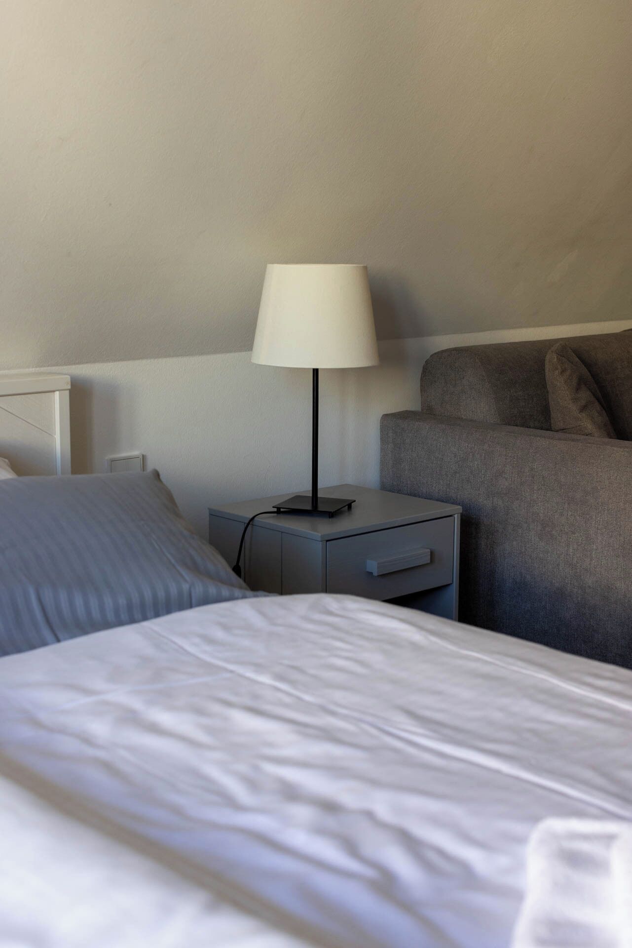 Ett hotellrum med en säng, ett nattduksbord med en lampa och en grå soffa.