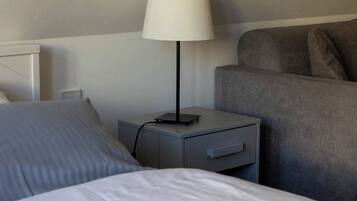 Ett hotellrum med en säng, ett nattduksbord med en lampa och en grå soffa.
