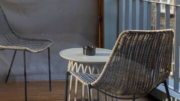 Ein Balkon mit zwei Korbstühlen, einem kleinen runden Tisch und einem Metallgeländer.