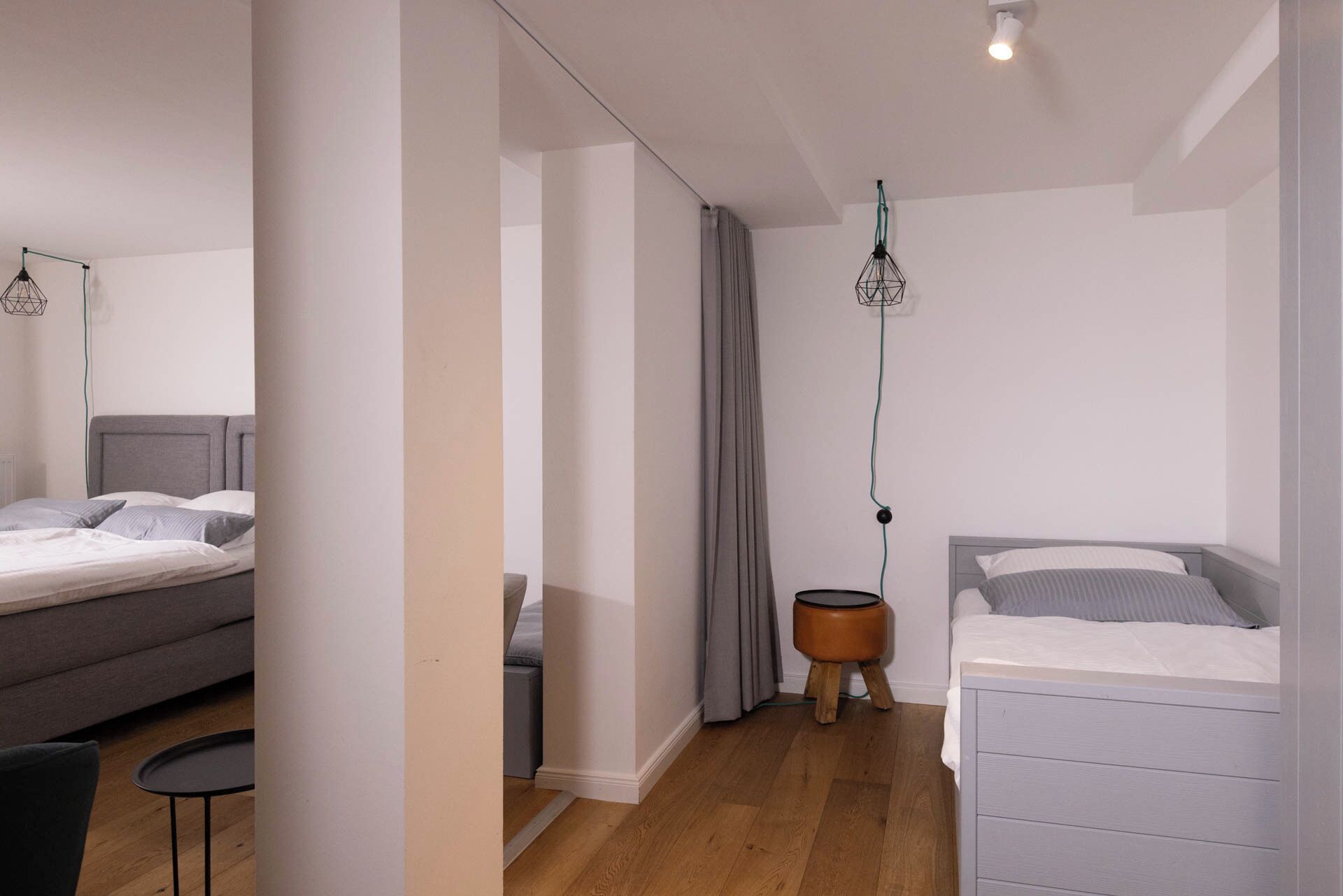 A modern bedroom with two beds, a small round table, and a hanging light fixture.
