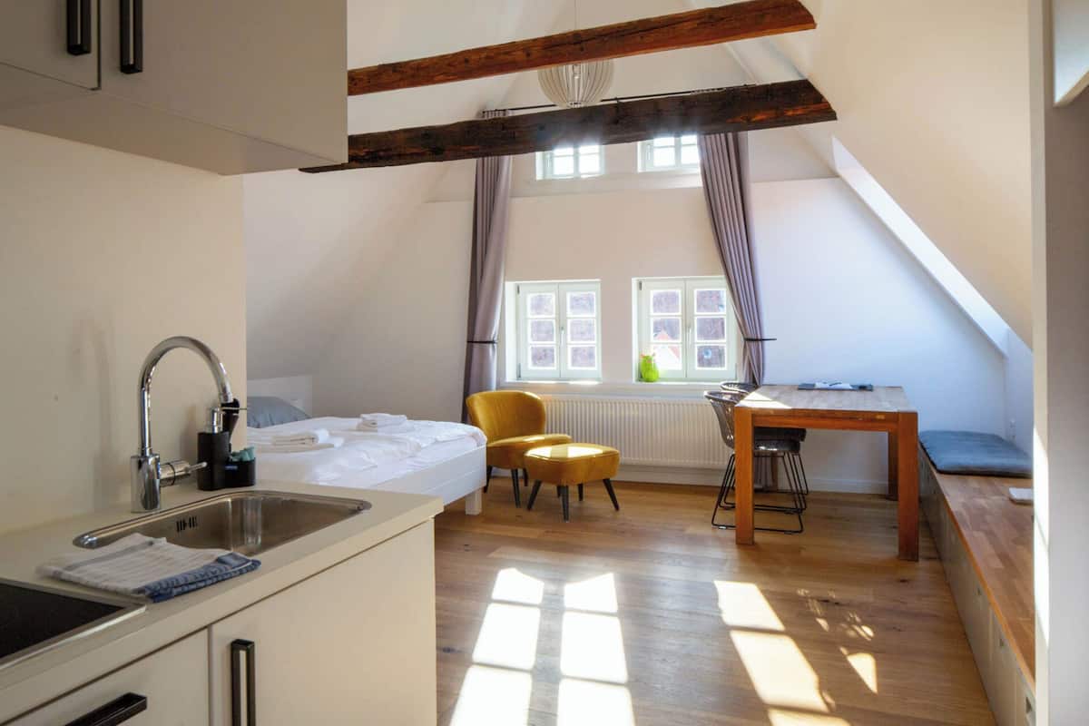A compact kitchen with a sink and stove, a dining area with a table and chairs, and a window with curtains.