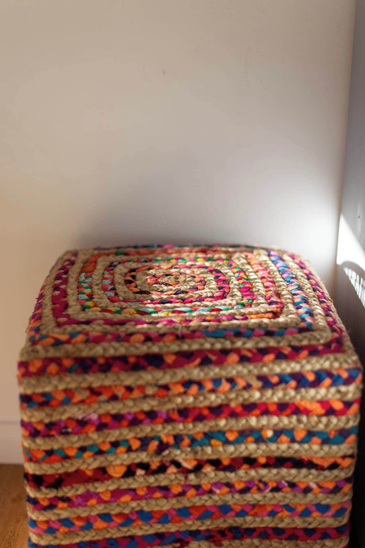 A square, multi-layered, colorful woven stool.