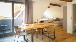 Ein modernes Loft-Apartment mit Esstisch aus Holz, Korbstühlen, einer Couch und einem Balkon mit Blick auf die Stadt.