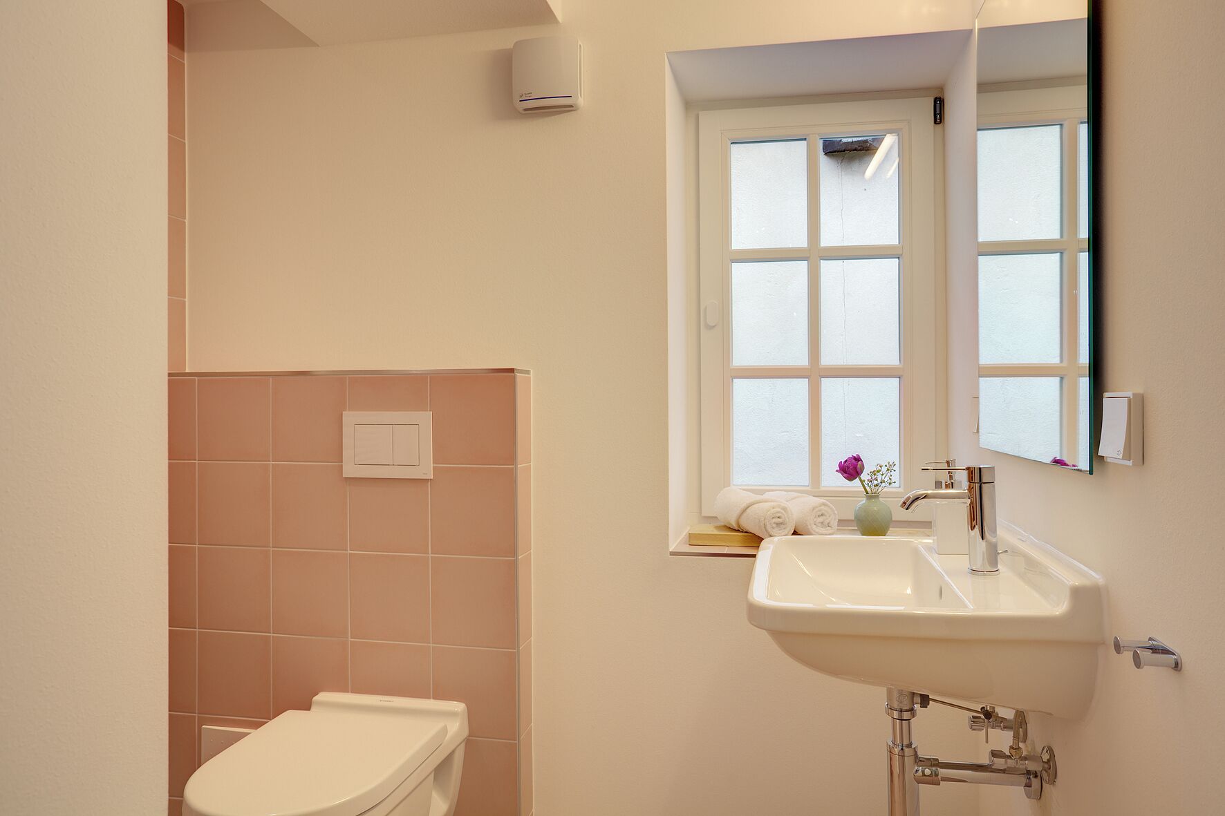 A bathroom with a toilet, sink, and window.