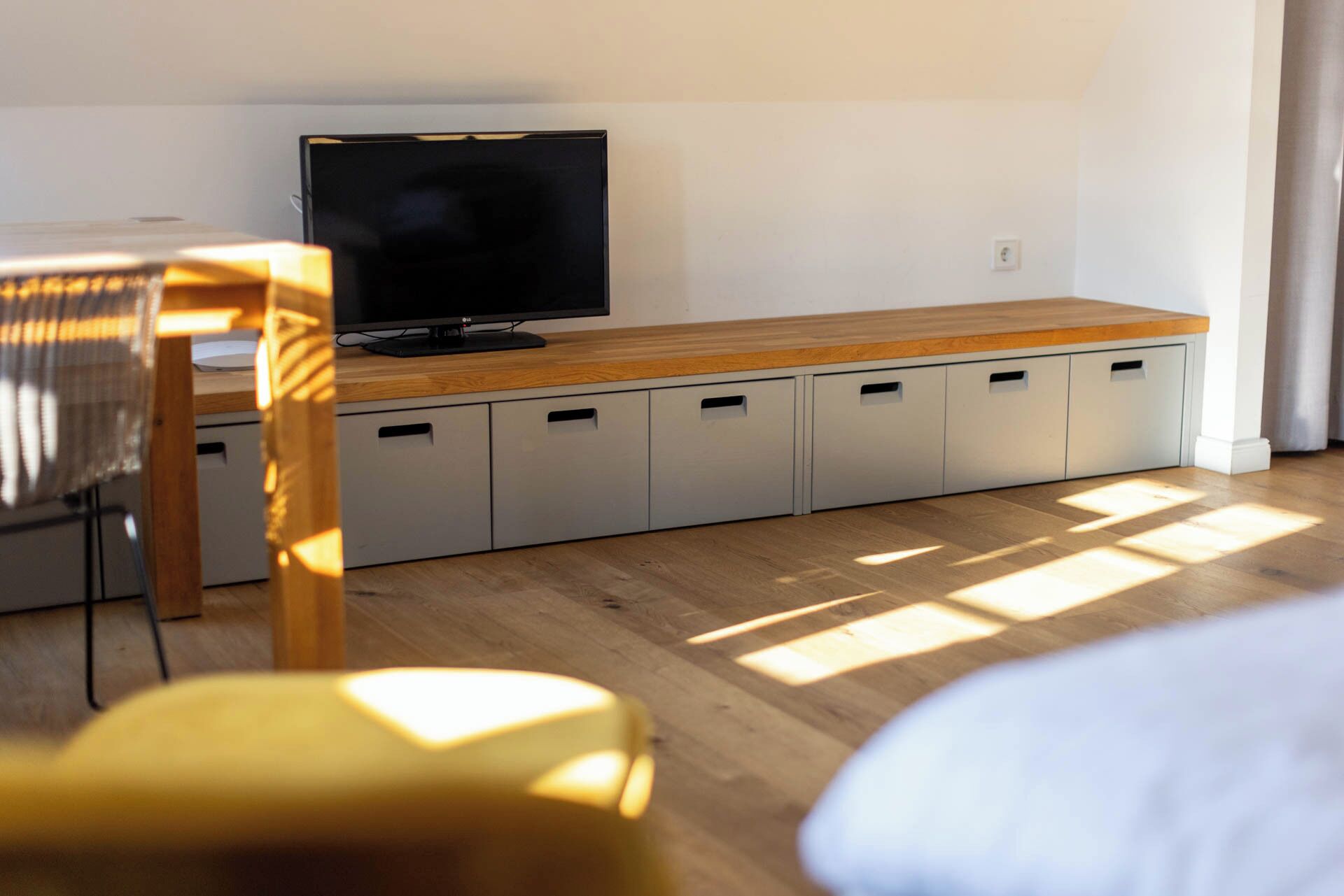 A room with a wooden desk, a television on a stand, and a built-in storage unit with multiple compartments.