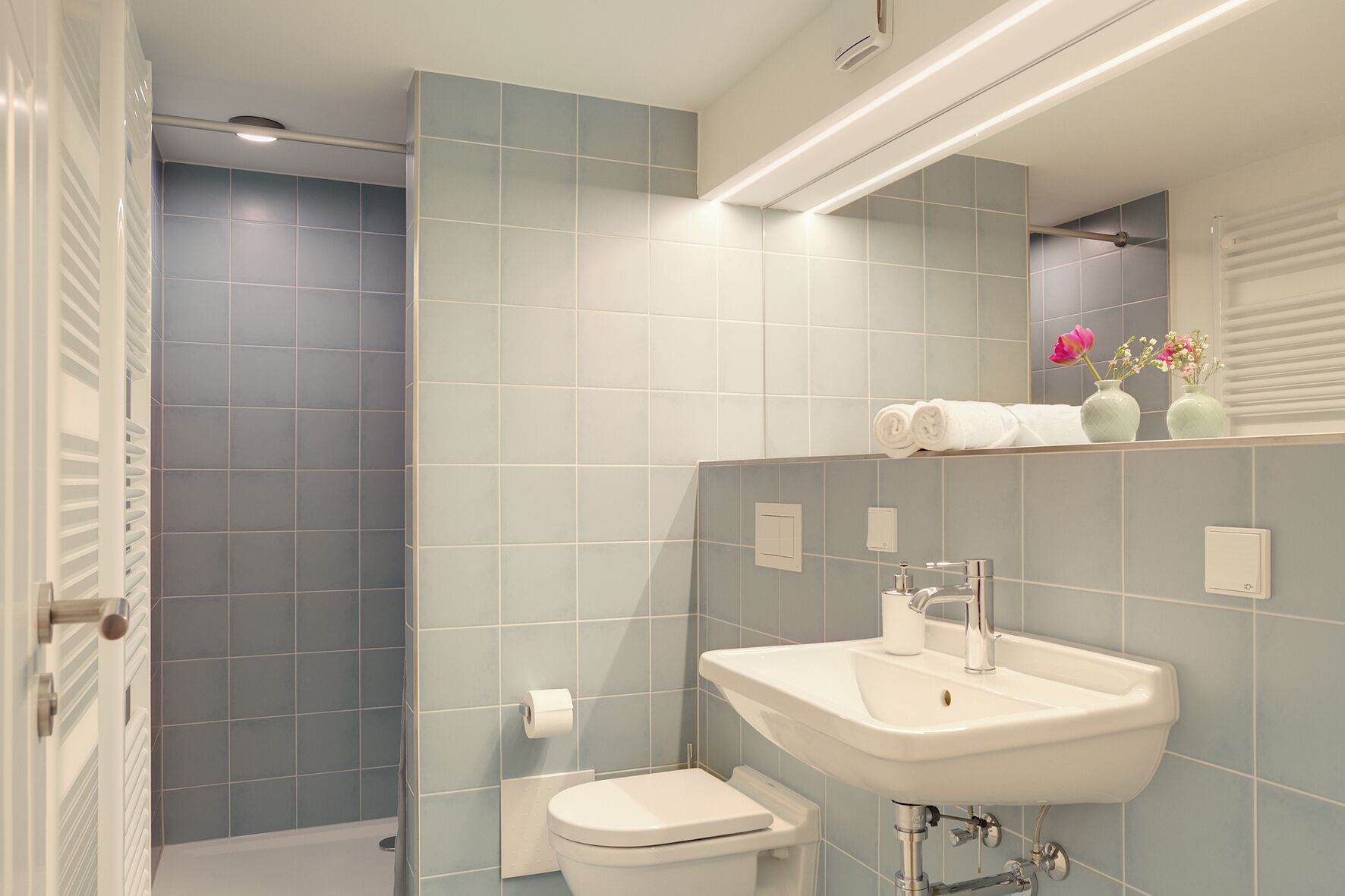Bagno con doccia, toilette, lavandino e specchio con ripiano sopra.