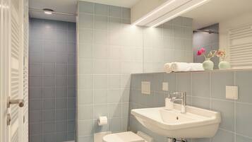 Bagno con doccia, toilette, lavandino e specchio con ripiano sopra.