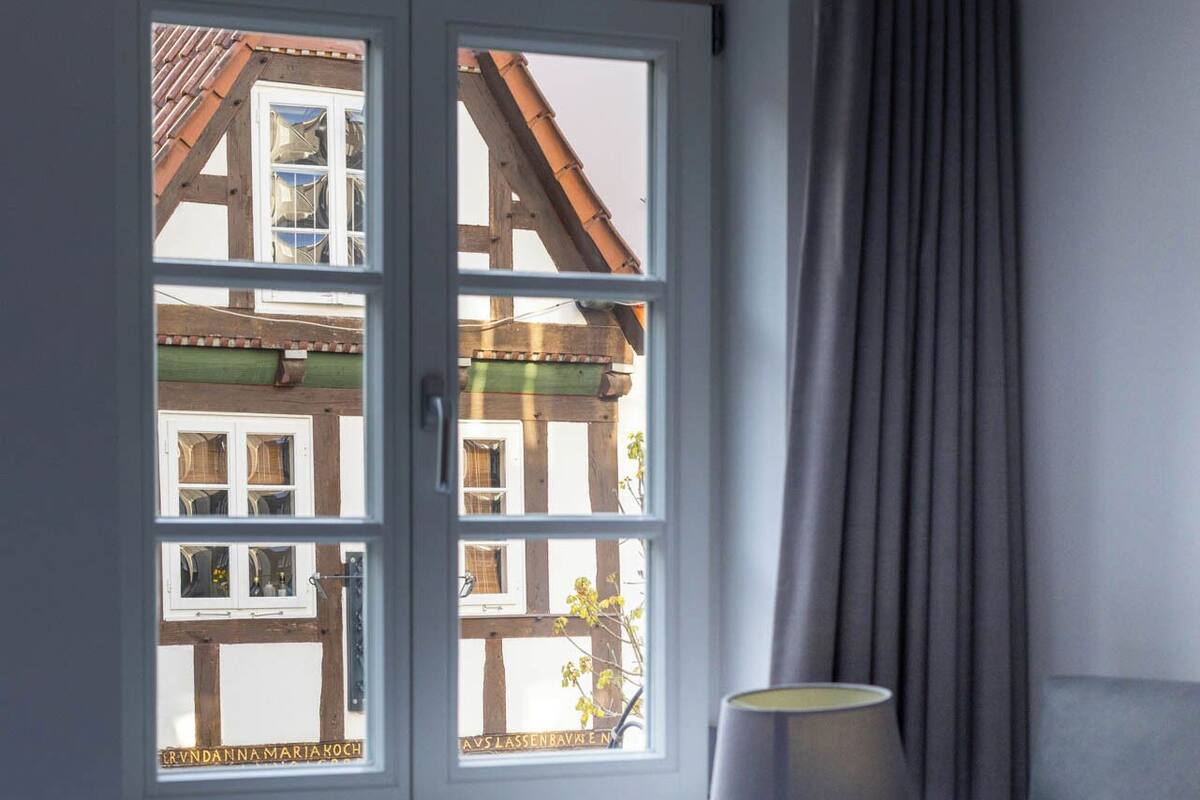 A hotel room with a bed, a window with a view of a traditional building, a lamp, and a curtain.