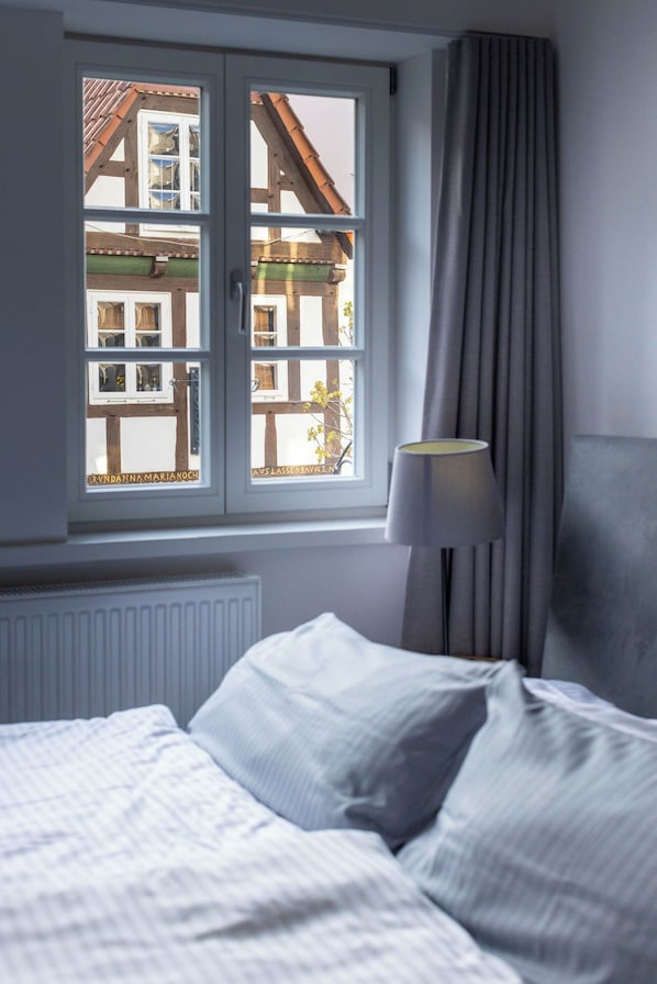 Una habitación de hotel con una cama, un ventanal que ofrece vistas a un edificio tradicional, una lámpara y una cortina.