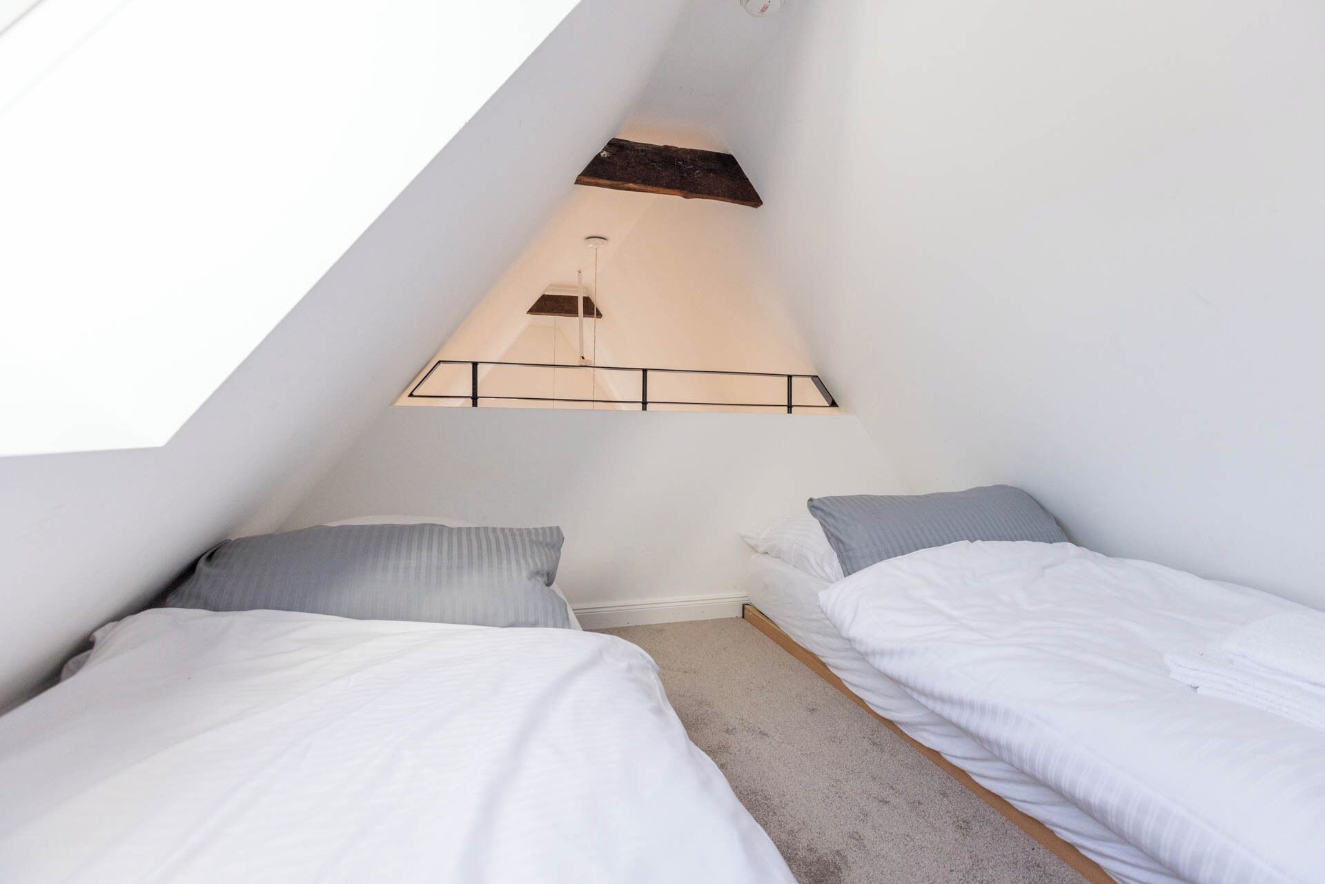 Une petite pièce aux murs inclinés, avec deux lits, un puits de lumière et un luminaire simple et moderne.