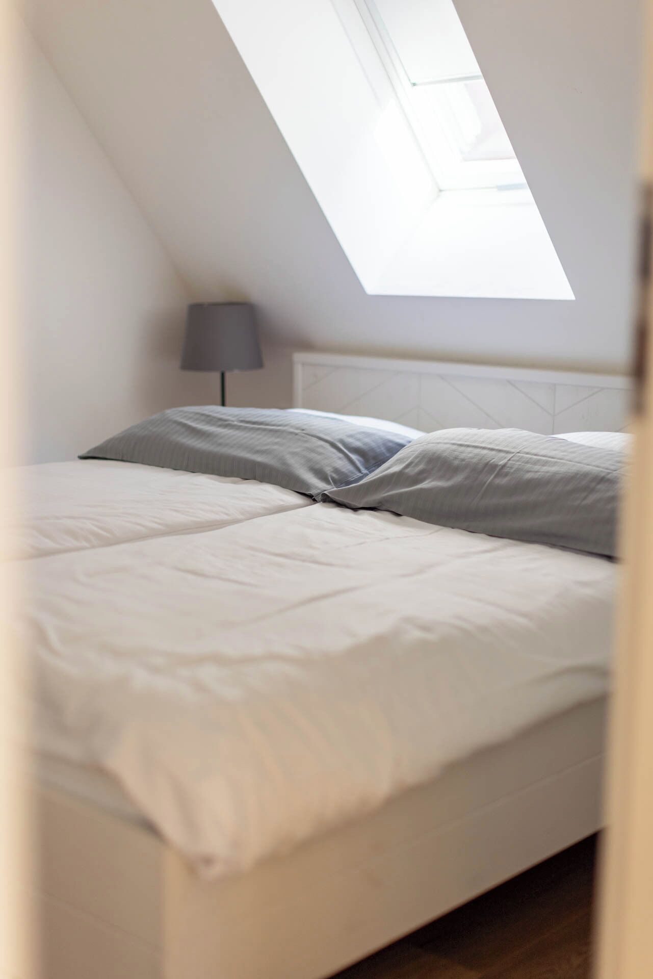 A bedroom with a bed, a lamp, and a skylight.