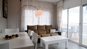 A modern living room with a sofa, a dining table, and a balcony with outdoor seating. - HomeHolidaysRentals  Maritim V (Pineda de Mar)