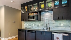 A modern kitchen with dark cabinetry, a microwave, and a tiled backsplash. - Bexley Bed and Breakfast (Columbus)