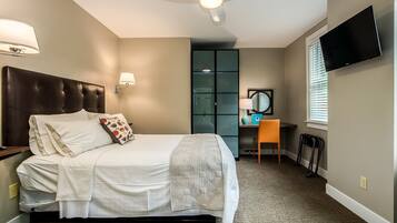 Een hotelkamer met een bed, een bureau, een stoel, een televisie en een plafondventilator.