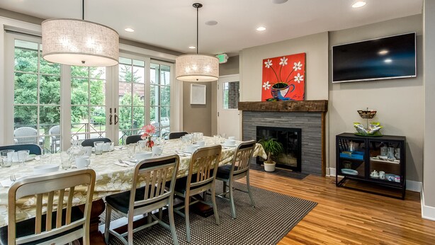 A dining area with a table set for six, a fireplace, and a television on the wall. - Bexley Bed and Breakfast (Columbus)