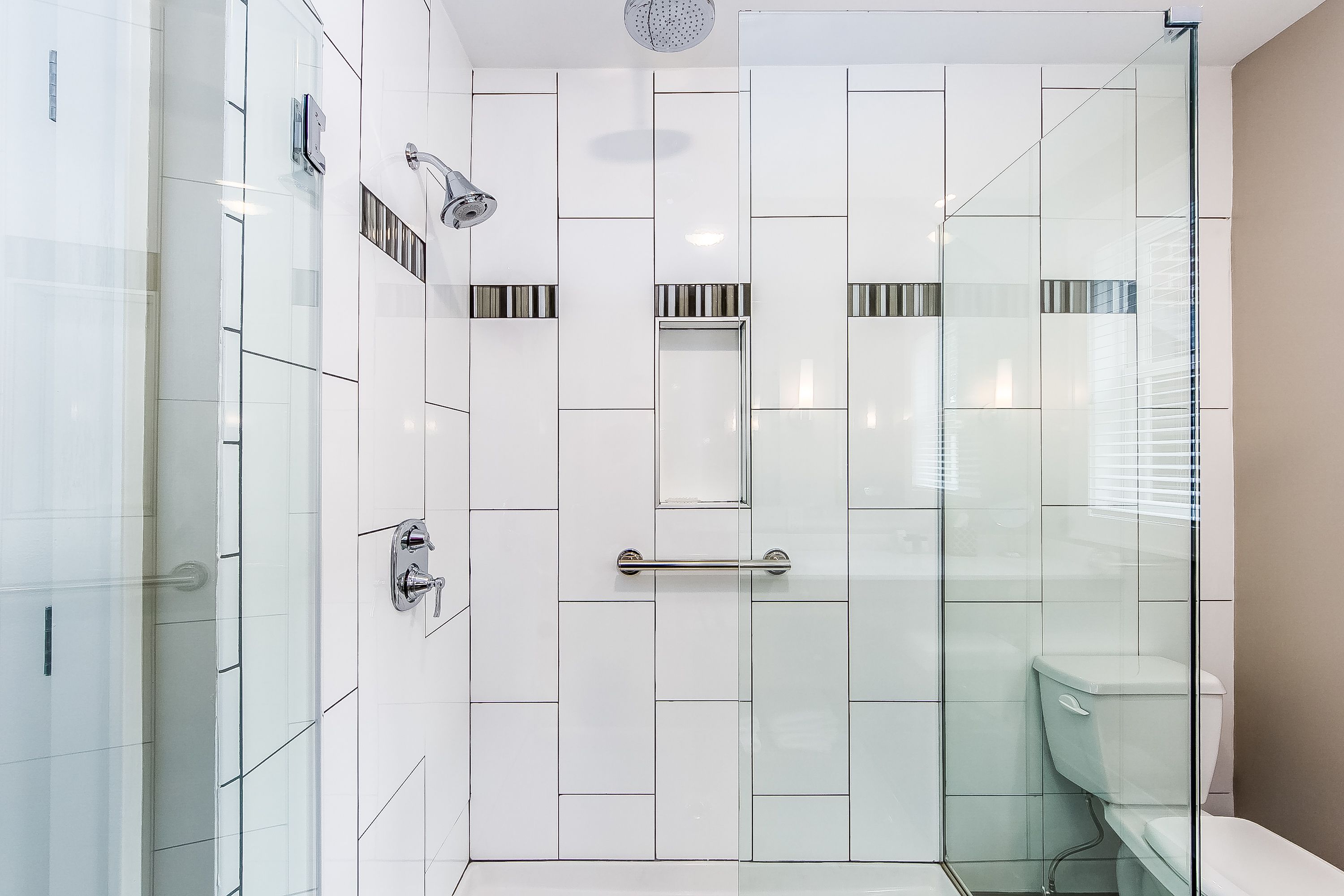 Ein modernes Badezimmer mit Duschkabine aus Glas, weißen Fliesenwänden und einer Toilette.