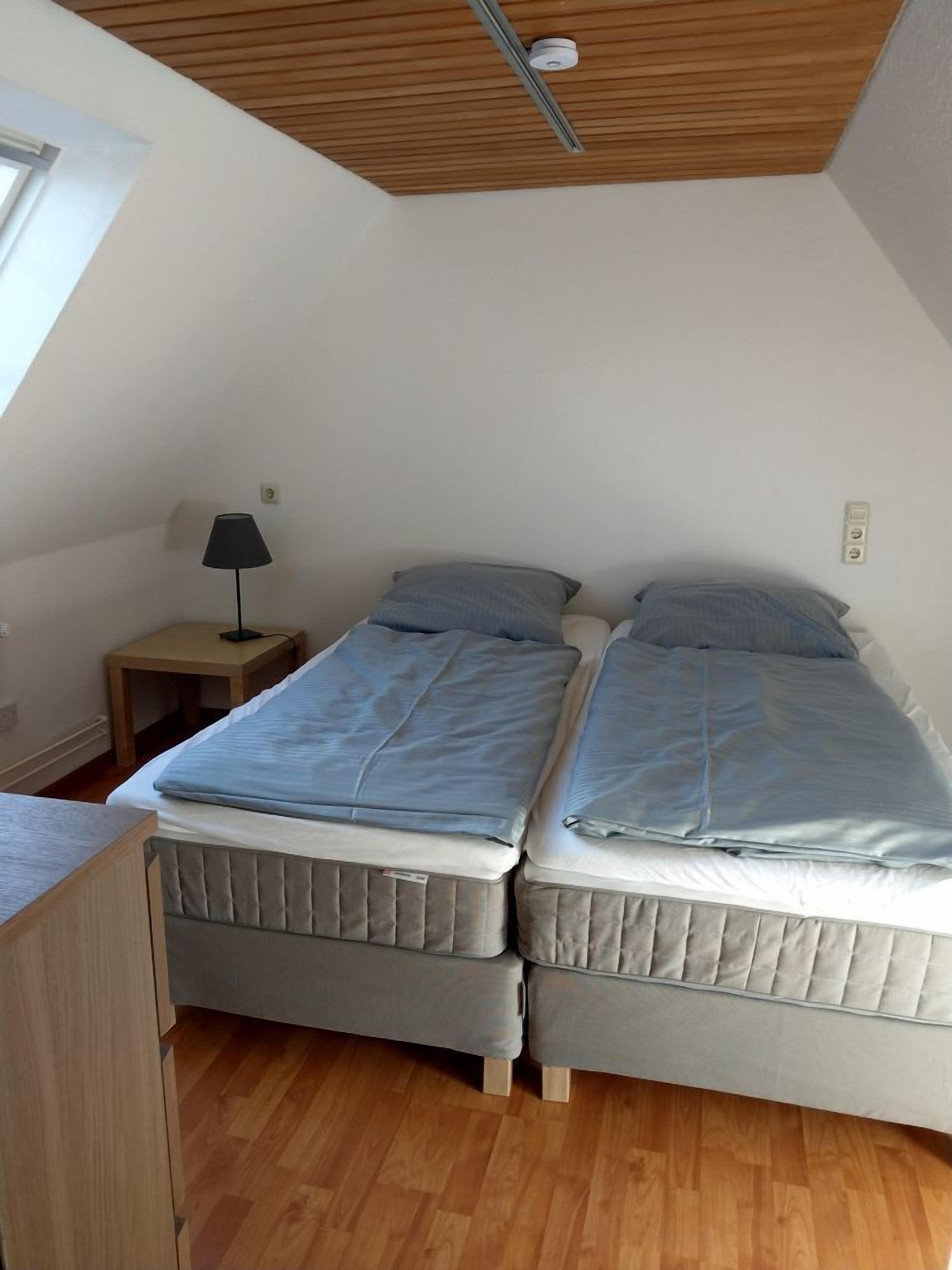 A bedroom with two beds, a nightstand, a lamp, and a ceiling light.