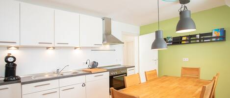 A modern kitchen with white cabinets, a wooden dining table, and pendant lights.